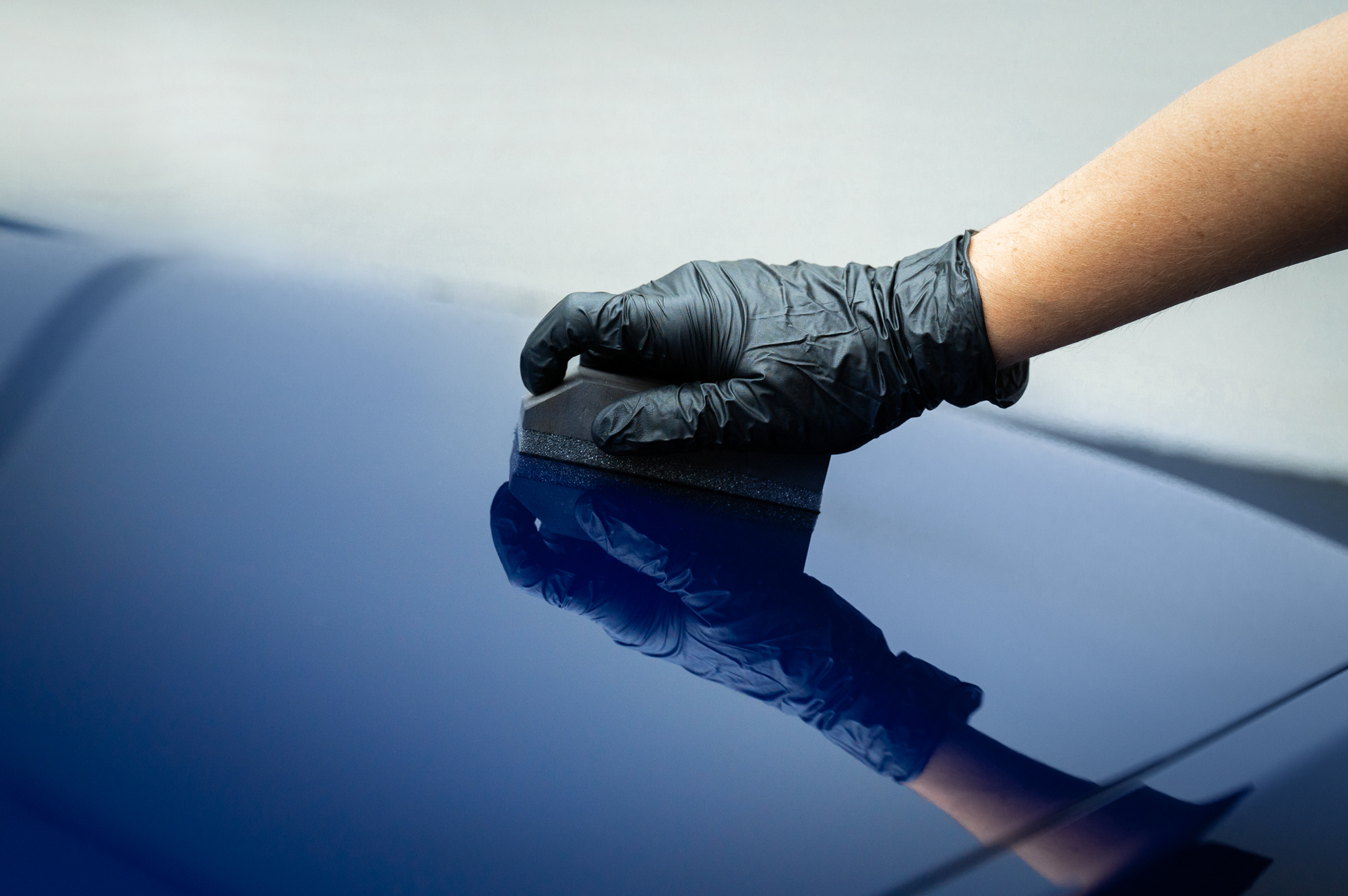 Gloved hand applying ceramic coating on a blue car surface